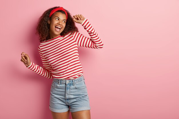 Adolescente ativa e energizada com cabelo encaracolado posando com um suéter vermelho listrado