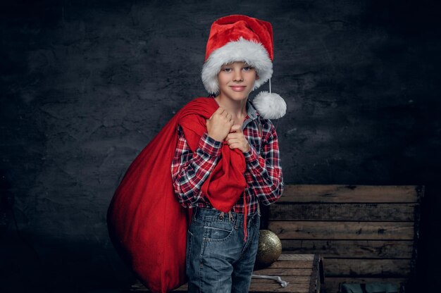 Adolescente bonito com chapéu de Papai Noel detém saco de presente de ano novo.