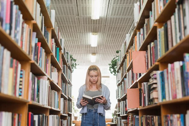 Adolescente bonito lendo entre estantes de livros