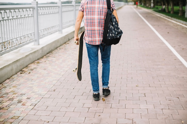 Adolescente com skate andando perto da cerca