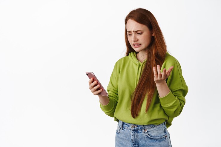 Foto grátis adolescente confusa olhando para smartphone com cara confusa, lendo mensagem estranha, erro de aplicativo no celular, encolhendo os ombros questionado, fundo branco