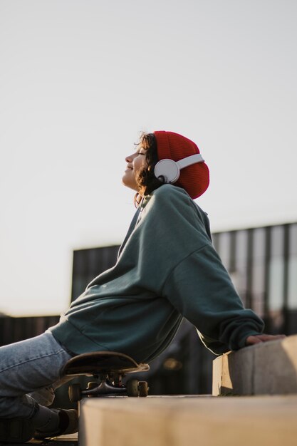 Adolescente curtindo música em fones de ouvido enquanto está sentado no skate