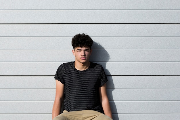 Adolescente do sexo masculino sentado e encostado na parede cinza