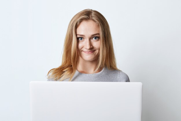 Adolescente fêmea que trabalha no computador, preapring para classes ou surfando nas redes sociais, olhando com expressão feliz na câmera isolada no branco. Modelo feminino usando gadget moderno