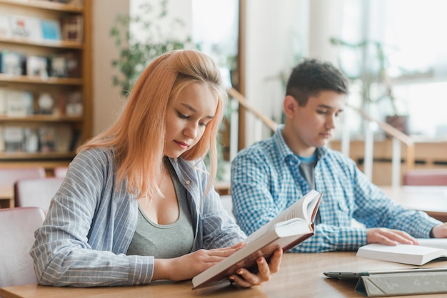 Adolescente lendo livro perto de amigo