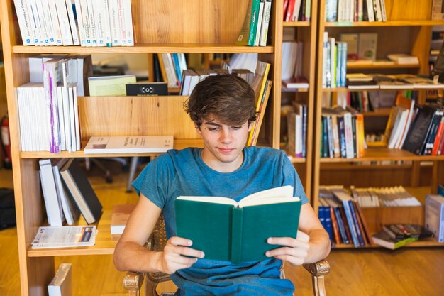 Adolescente masculino alegre lendo na cadeira