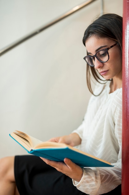 Adolescente mulher lendo livro sentado na escada na biblioteca