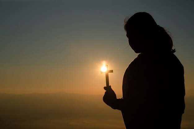 Adolescente que guarda a cruz com rezar. Paz, esperança, conceito de sonhos.