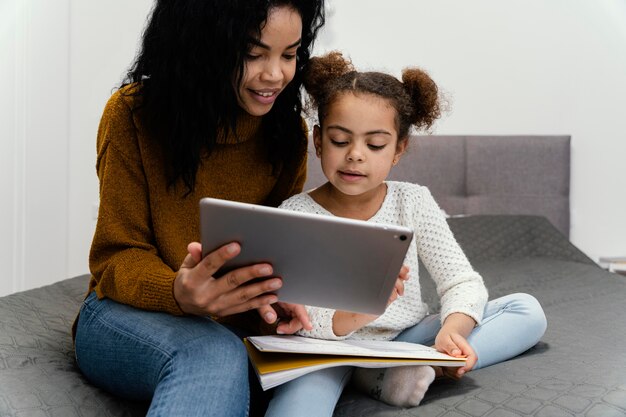 Adolescente sorridente ajudando a irmãzinha usando um tablet para a escola online