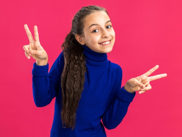 Adolescente sorridente fazendo o sinal da paz isolado na parede rosa