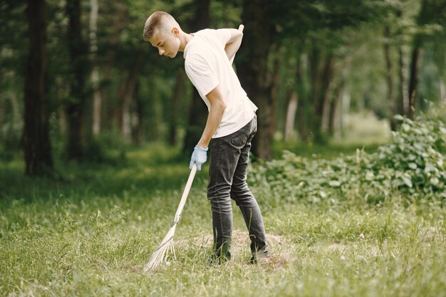 Adolescente voluntário. Menino europeu em luvas pegando garrafas plásticas em um saco de lixo preto ao ar livre.