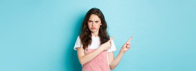 Foto grátis adolescente zangada franzindo a testa e mal-humorada com desaprovação enquanto apontava para a esquerda para uma má e injusta fina