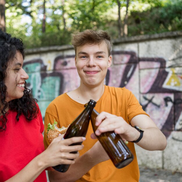 Adolescentes torcendo por garrafas e comendo hambúrguer ao ar livre