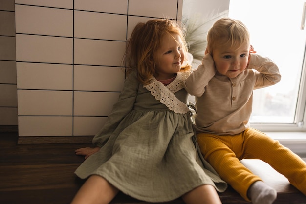 Adoráveis bebês de pele clara, menina ruiva e menino loiro em roupas de casa estão dentro de casa conceito de família amigável