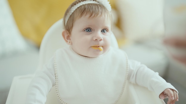 Foto grátis adorável bebê loiro sentado na cadeira comendo em casa