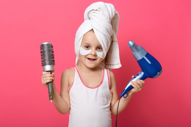 Adorável criança do sexo feminino segurando o secador de cabelo e pente nas mãos