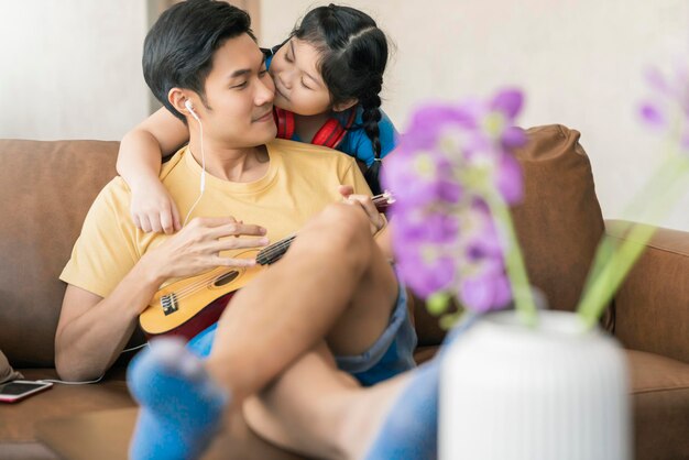 Adorável família asiática pai e filha passaram o tempo de quarentena de fim de semana tocando instrumento ukulele e cantando junto com fundo interior de casa divertido e alegre