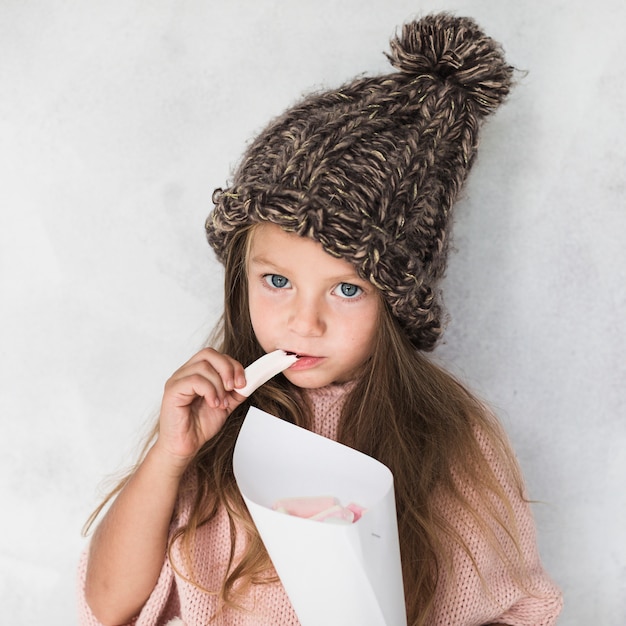 Adorável garota comendo e usando chapéu de inverno