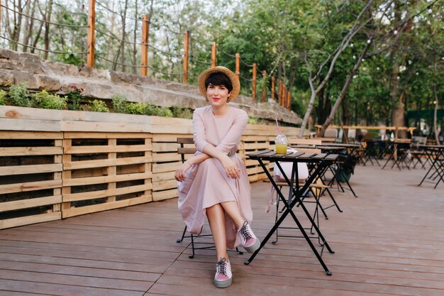 Adorável garota elegante de cabelos curtos descansando no restaurante do parque, aproveitando o fim de semana no dia de verão
