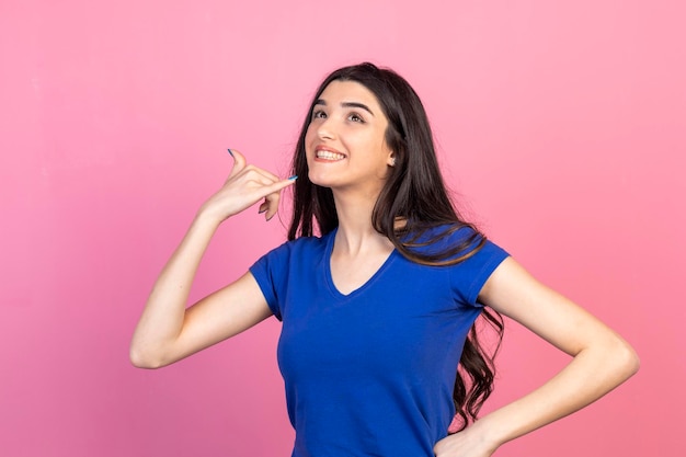 Adorável garota gesticulando telefone com a mão e sorrindo