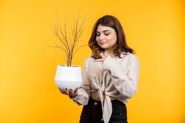 Foto grátis adorável garota segurando o vaso de flores e apontar o dedo nele foto de alta qualidade