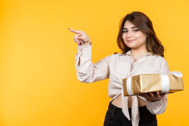 Adorável garota segurando sua caixa de presente e apontar o dedo de lado Foto de alta qualidade