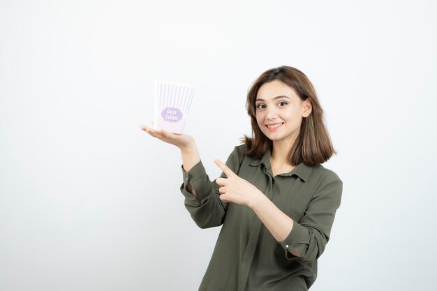 Adorável jovem apontando para caixa de pipoca e posando. Foto de alta qualidade