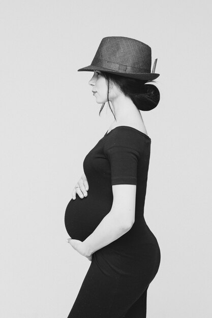 Adorável jovem mãe de vestido preto posando para a câmera com a barriga, foto em preto e branco isolada no fundo branco