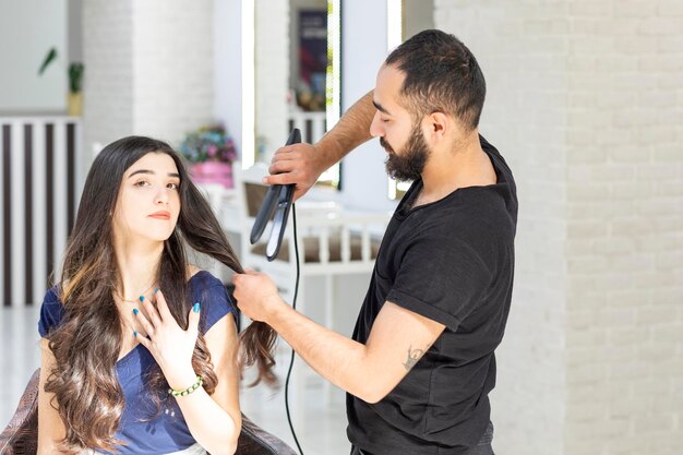 Adorável jovem sentada em uma cadeira e barbeiro usando secador de cabelo para moldar seu cabelo Foto de alta qualidade