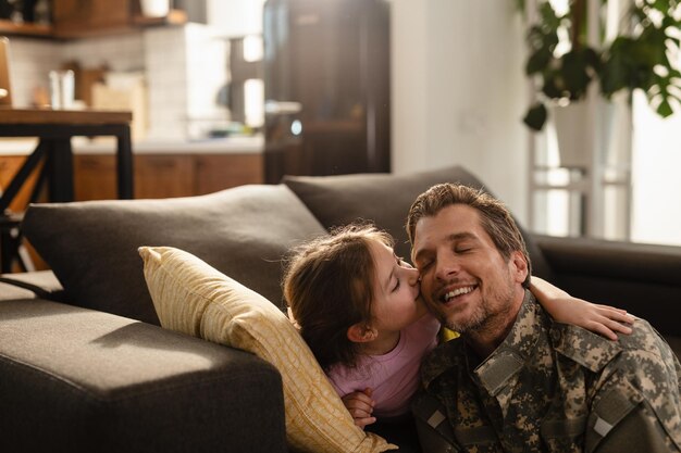 Adorável menina beijando seu pai militar na sala de estar