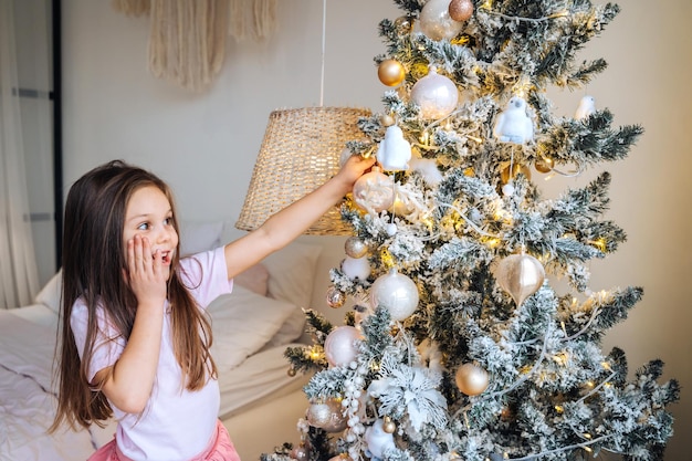Adorável menina decorando uma árvore de natal com bugigangas em casa