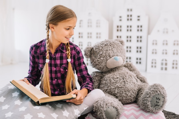 Adorável menina lendo um livro com seu ursinho de pelúcia