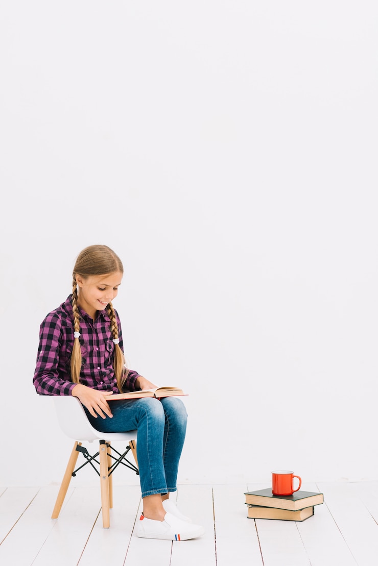 Foto grátis adorável menina sentada em uma cadeira lendo um livro