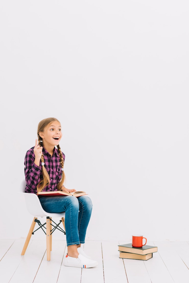 Foto grátis adorável menina sentada em uma cadeira lendo um livro