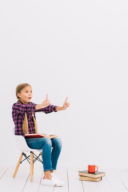 Adorável menina sentada em uma cadeira lendo um livro