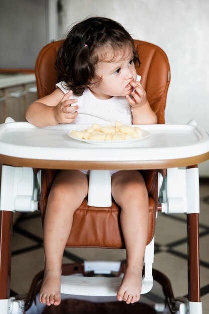 Adorável menina sentada na cadeira de criança e comer