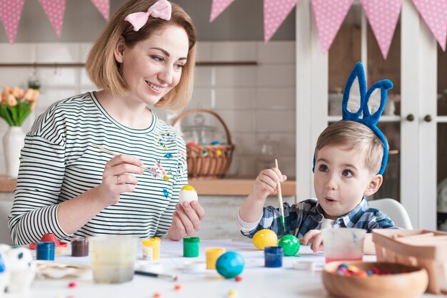 Adorável menino pintando ovos de Páscoa com a mãe