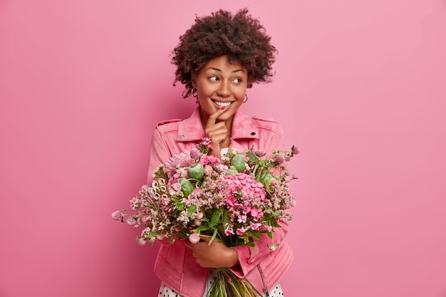 Adorável mulher alegre olha para o lado, pega um buquê de flores, olha feliz para o lado, posa