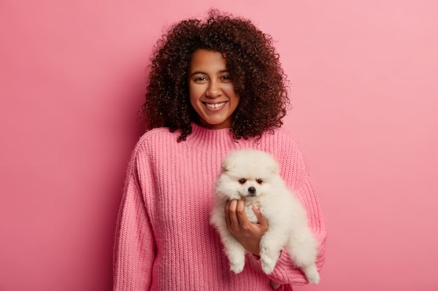 adorável senhora de pele escura em um suéter de tricô, sendo amiga do cachorro, usa um suéter rosa