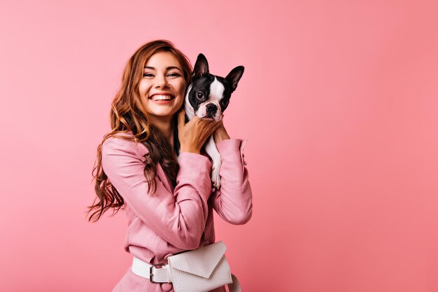 Adorável senhora ruiva posando com buldogue francês e sorrindo Retrato de estúdio de menina rindo elegante segurando cachorrinho e olhando para a câmera