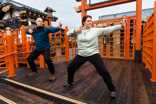 Adultos de tiro completo praticando tai chi lá fora