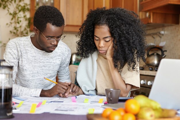 Africano, deprimido, desempregado, usando óculos e muitas dívidas segurando a mão de sua esposa infeliz