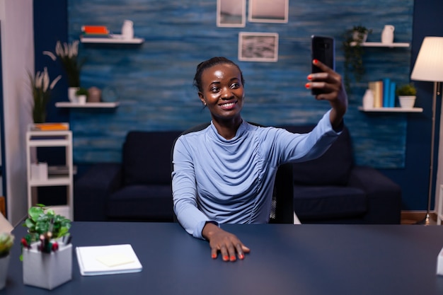 Africano feliz olhando para smartphone tomando selfie olhando para a câmera frontal. Freelancer com foco ocupado usando moderna rede de tecnologia sem fio fazendo horas extras.