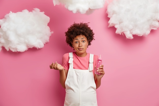 Afro-americana futura mãe aguarda poses de criança com grande abdômen estando no terceiro trimestre sem saber segurando mamadeira vestida com roupas para carrinhos de grávidas