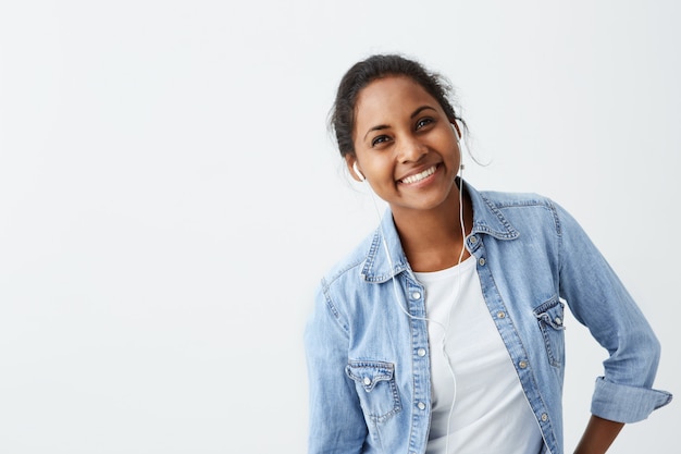 Foto grátis afro-americano fêmea bonito na camisa azul com sorriso sincero, regozijando-se com seu sucesso no trabalho, com bom humor, mostrando suas emoções positivas. pessoas, felicidade, expressões faciais e emoções.