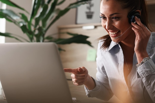 Foto grátis agente de atendimento ao cliente feliz com fone de ouvido se comunicando com um cliente e trabalhando no laptop no call center