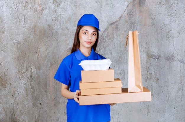Agente de serviço feminino de uniforme azul segurando caixas de papelão, caixas de compras e caixas para viagem