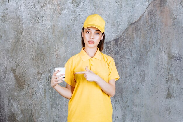 Agente de serviço feminino em uniforme amarelo, segurando um copo de plástico.