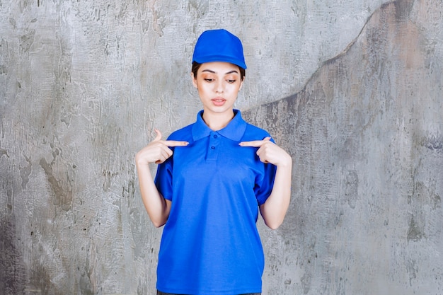 Foto grátis agente de serviço feminino em uniforme azul, apontando para si mesma.