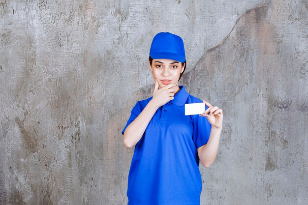 Agente de serviço feminino em uniforme azul, apresentando seu cartão de visita e parece confusa ou pensativa.